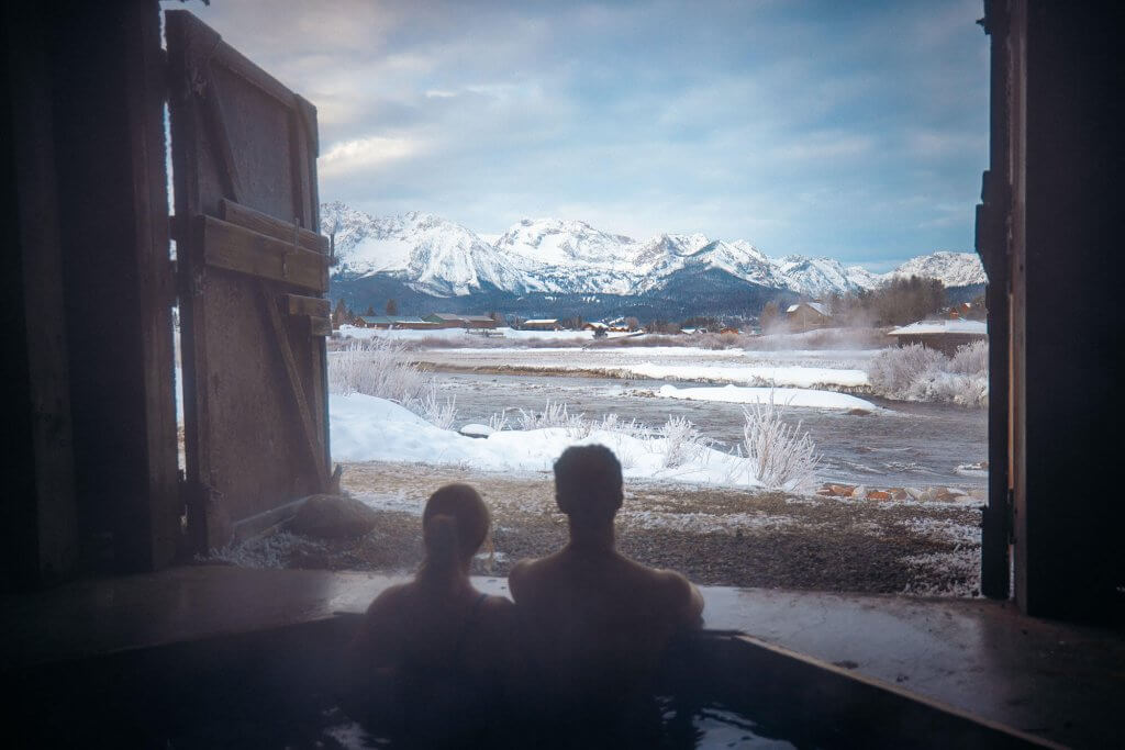 Two people enjoy steamy hot springs with mountain views.