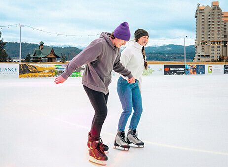 Two ice skaters holding hands on ice rink.