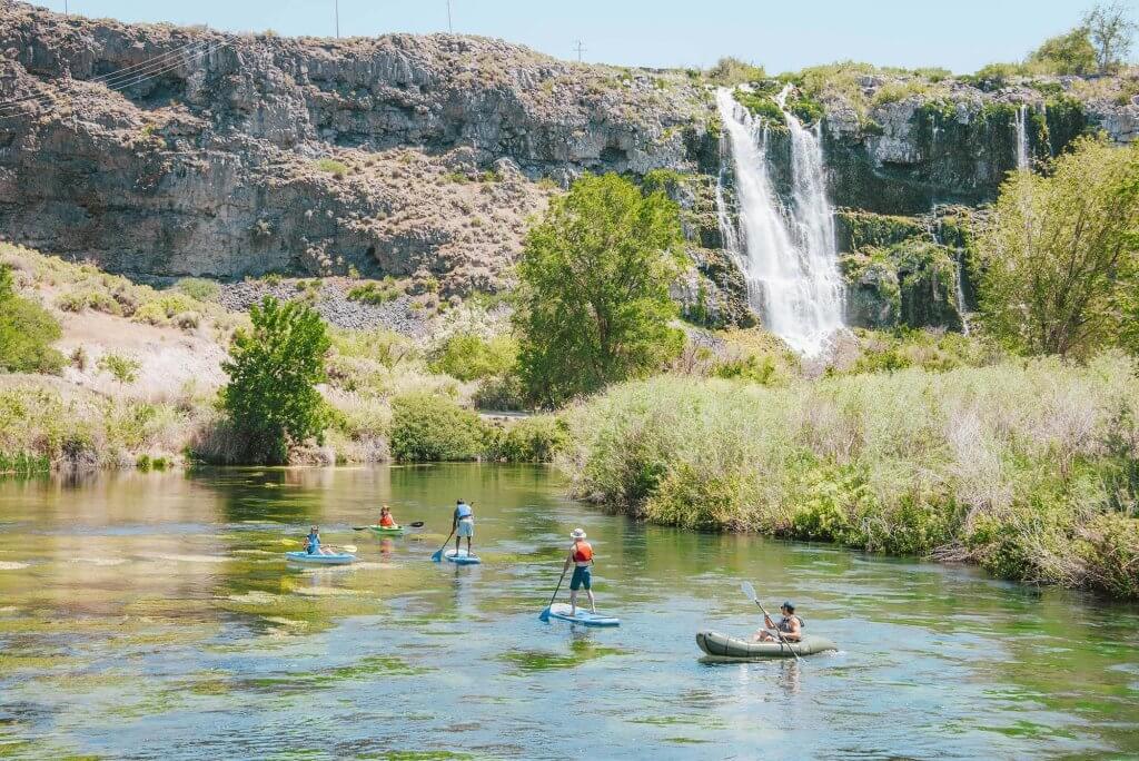 People paddleboarding and kayak near a waterfall at Ritter Island in Thousand Springs State Park.