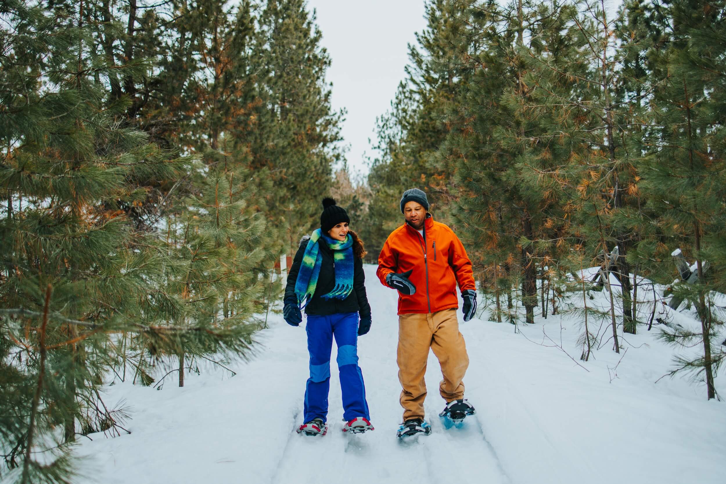 A couple goes snowshoeing down the Crown Point Railroad Grade Trail, surrounded by trees.