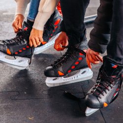 Two people sitting down and lacing up their ice skates.