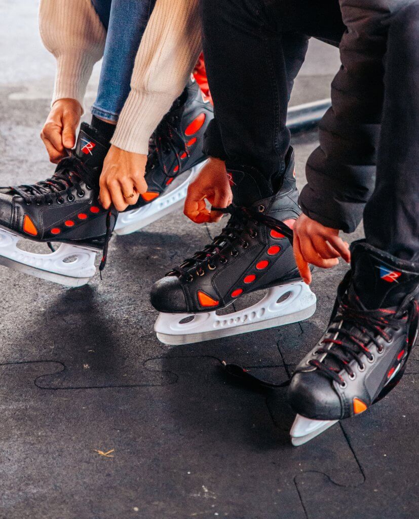 Two people sitting down and lacing up their ice skates.