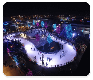 An aerial view of people skating at Indian Creek Plaza Ice Skating Ribbon surrounded by trees with colorful lights.