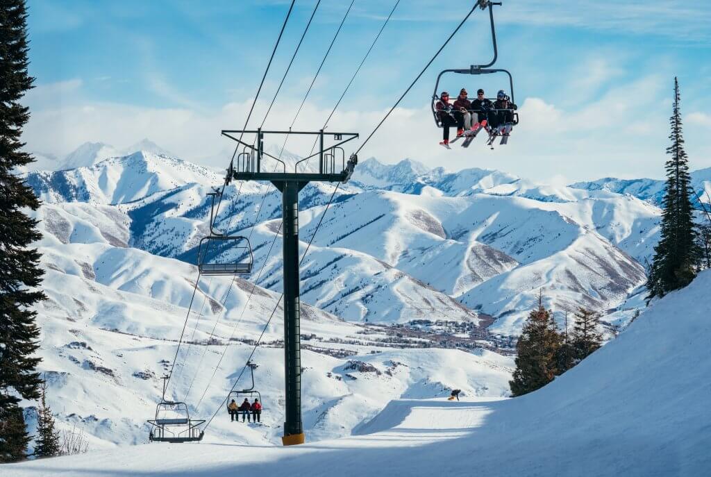 Groups of people riding a chair lift at Sun Valley Resort, surrounded by snow-covered landscapes and trees.