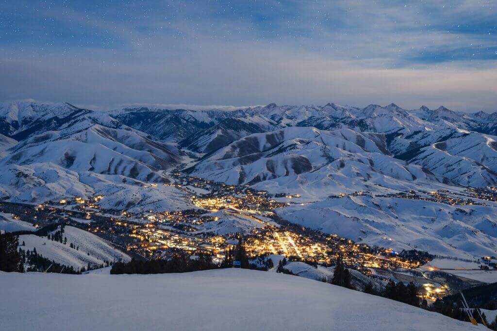 A scenic overlook showing the town of Sun Valley at night, lit up with lights surrounded by snow-covered mountains. 