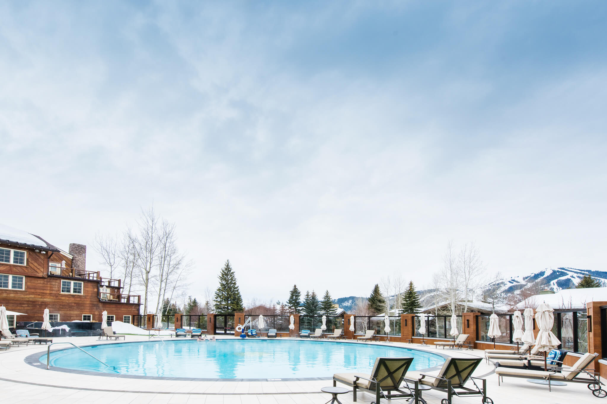 A large round pool surrounded by pool chairs and folded umbrellas and a wooden building in the background at Sun Valley Lodge.