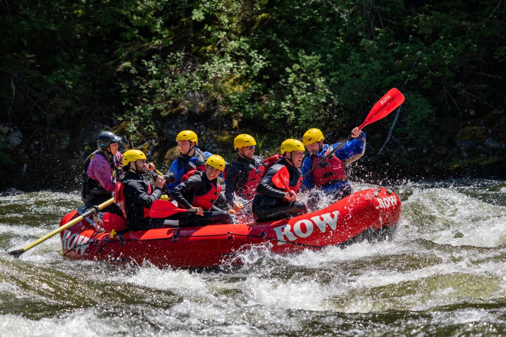 Smiling rafters in a red ROW Adventures raft splashing through whitewater on the Lochsa River