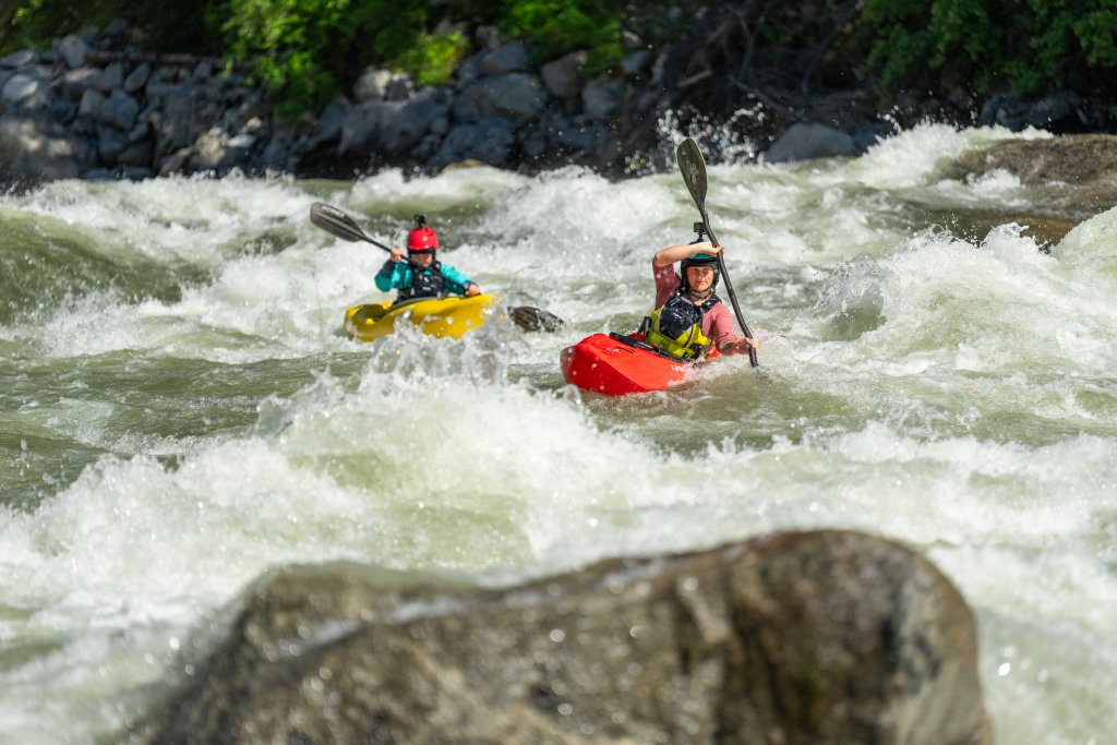 Two kayakers paddle through a fast-moving section of whitewater on the Payette River.