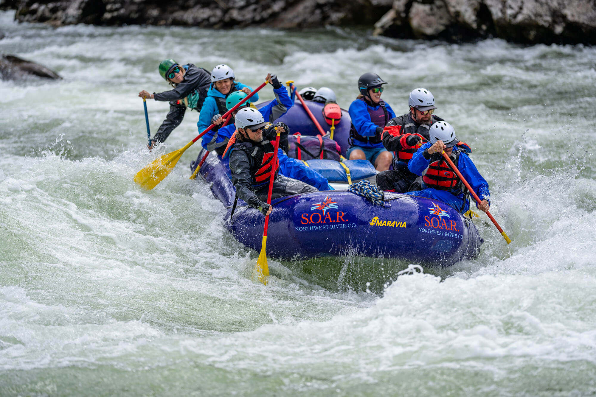 A group in helmets goes whitewater rafting on the Selway River with SOAR Northwest, oars mid-splash.