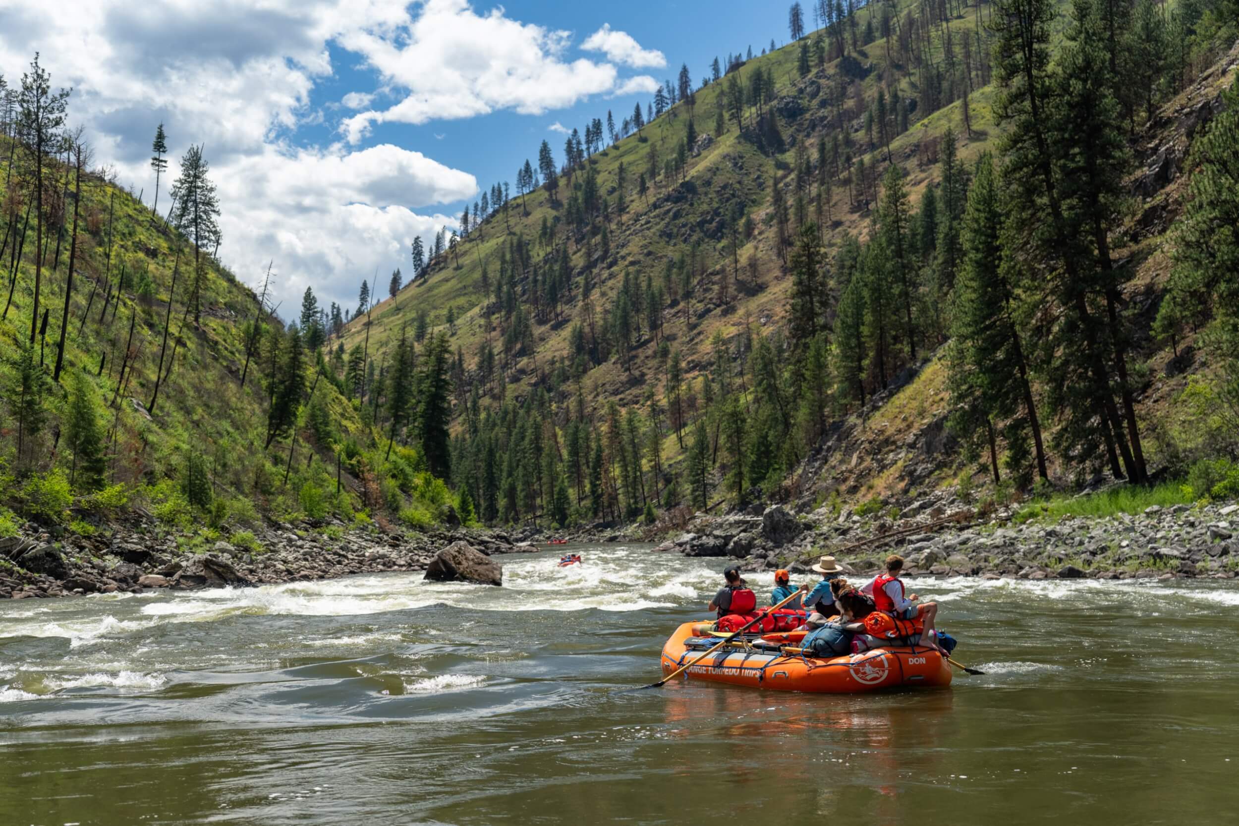 Rafters with Orange Torpedo Trips floating down the Main Salmon River surrounded by steep forested slopes