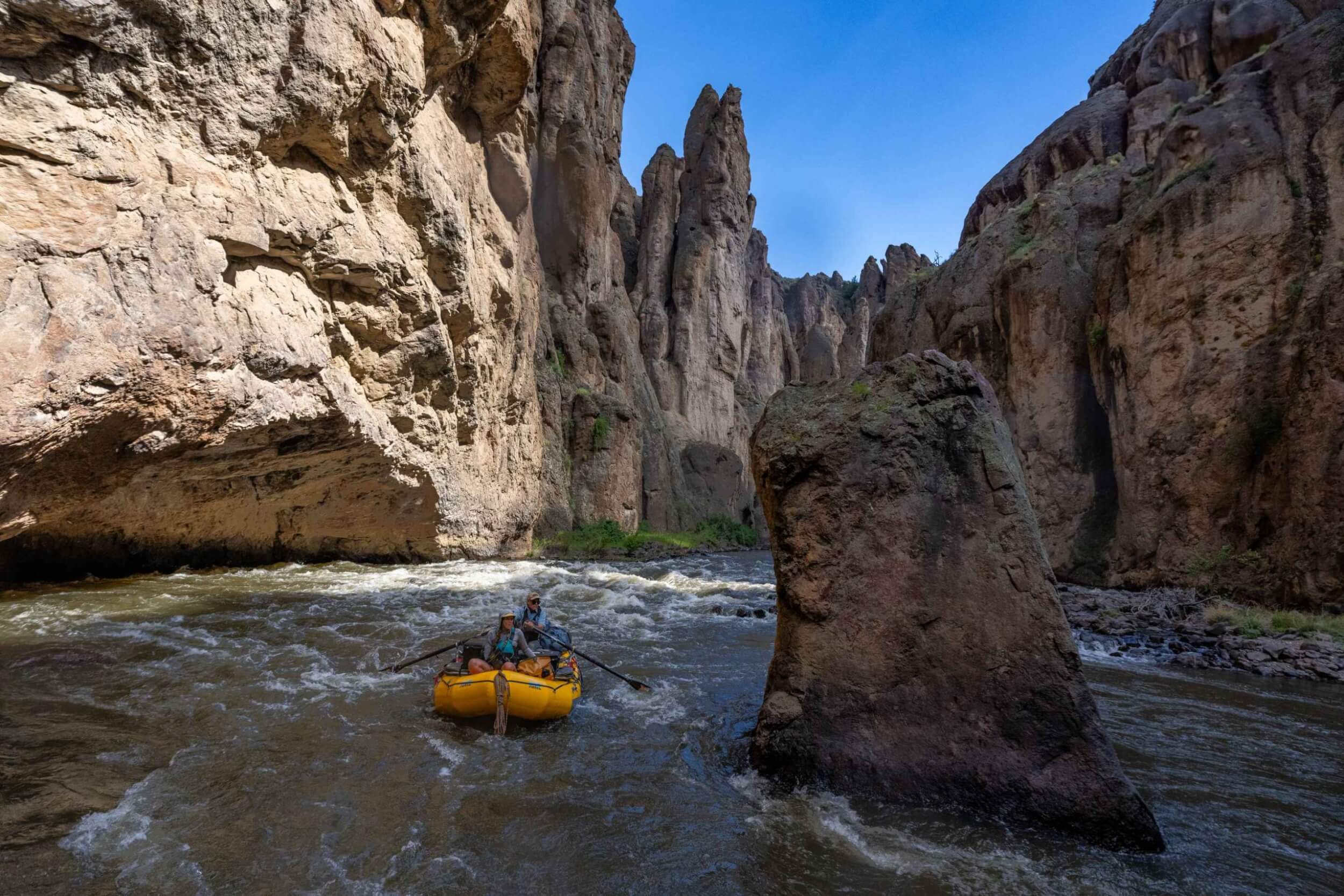 Yellow raft enters a narrow gorge surrounded by towering canyon walls.