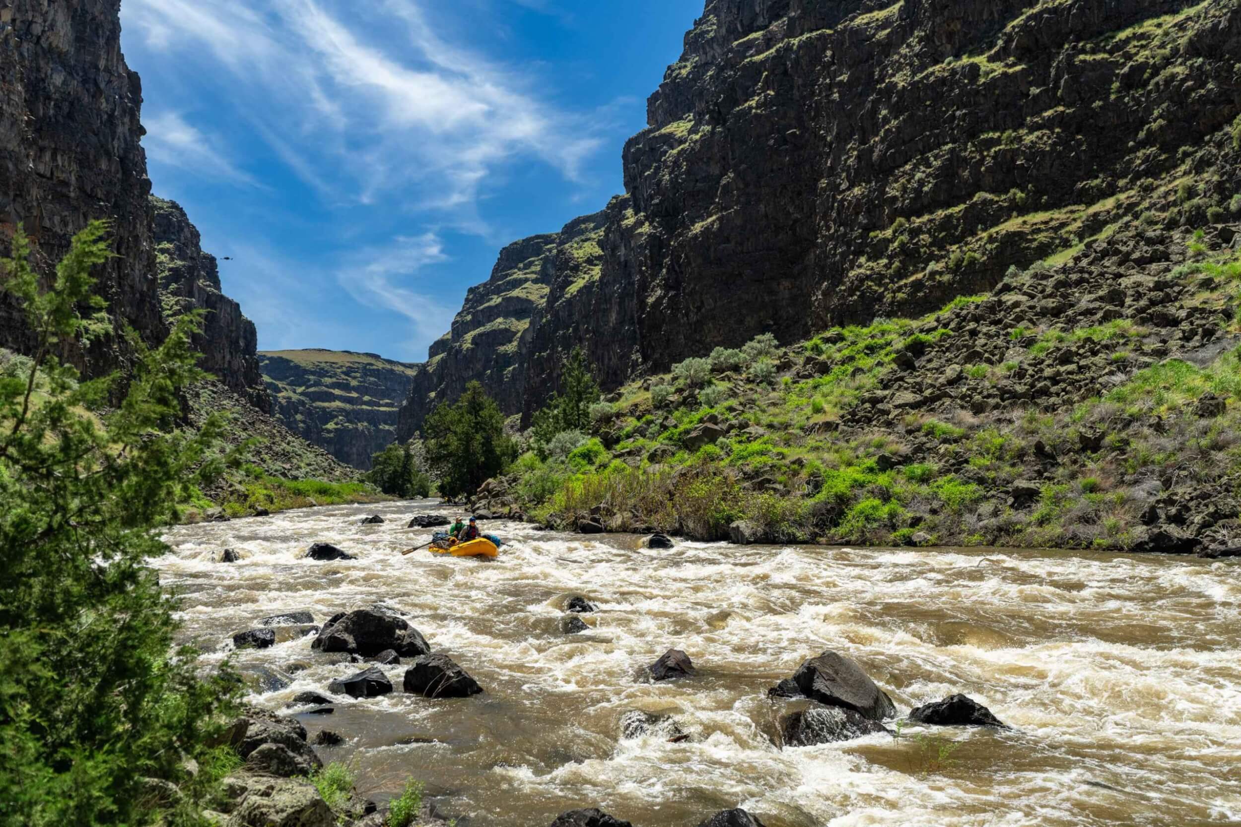 Rafters navigate whitewater between steep volcanic walls under a blue sky.