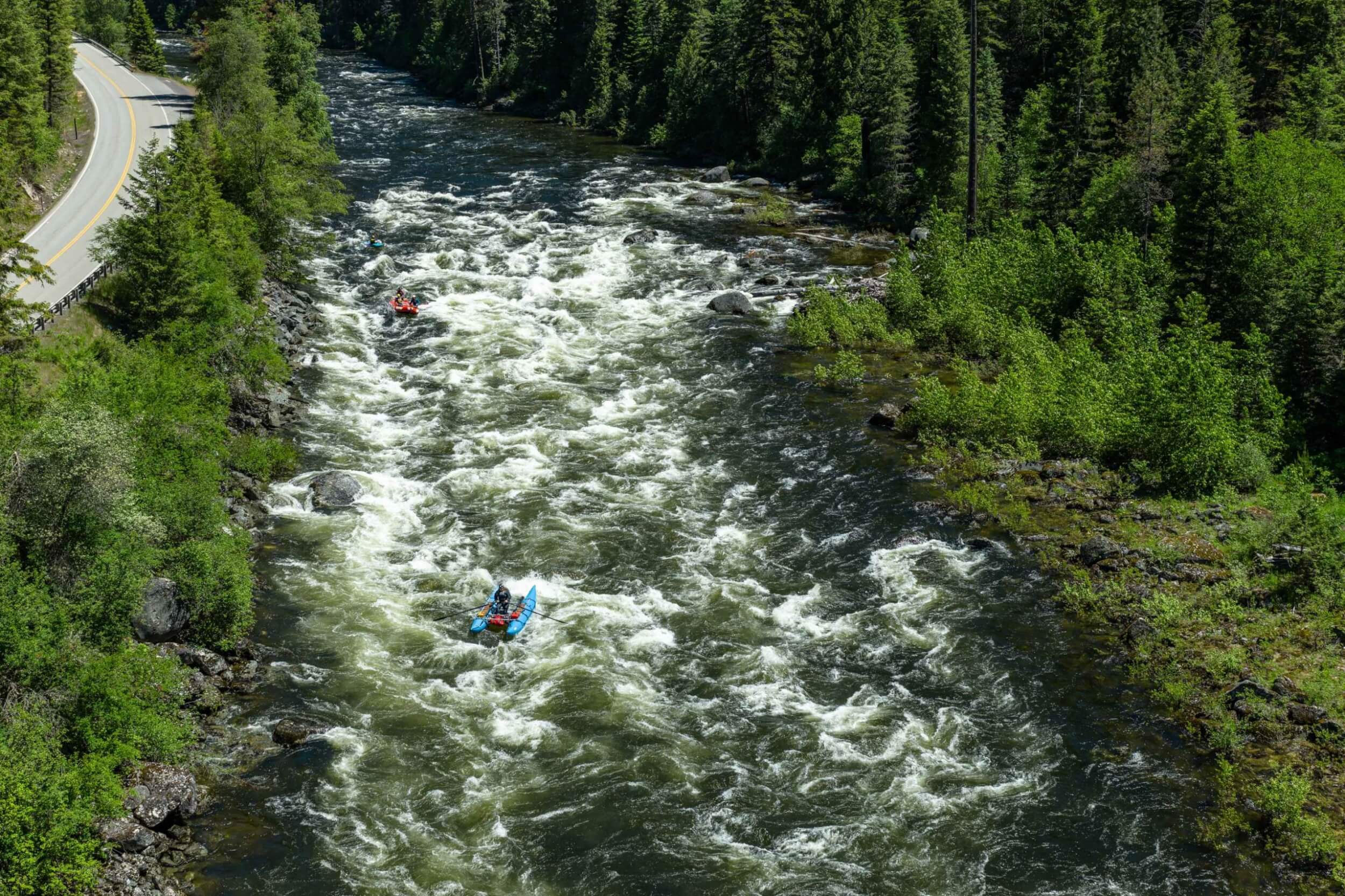 Multiple rafts and kayaks descend a rapid-lined stretch of the St. Joe River