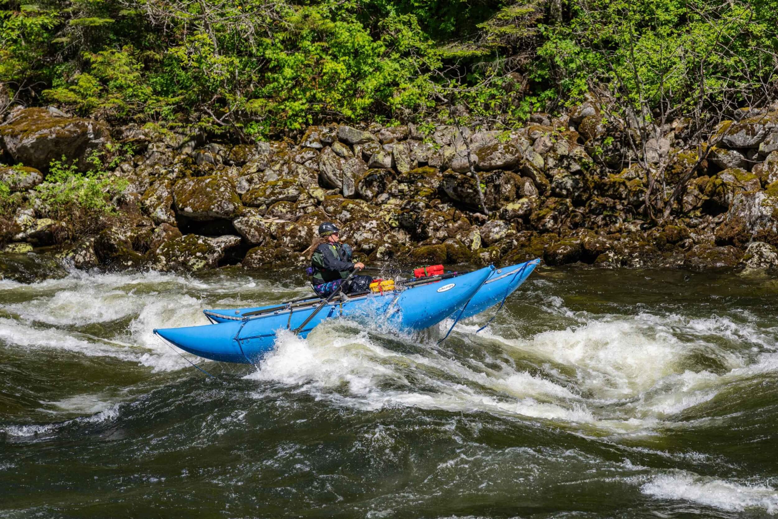 Single rafter rows a blue cataraft through a rocky section of river