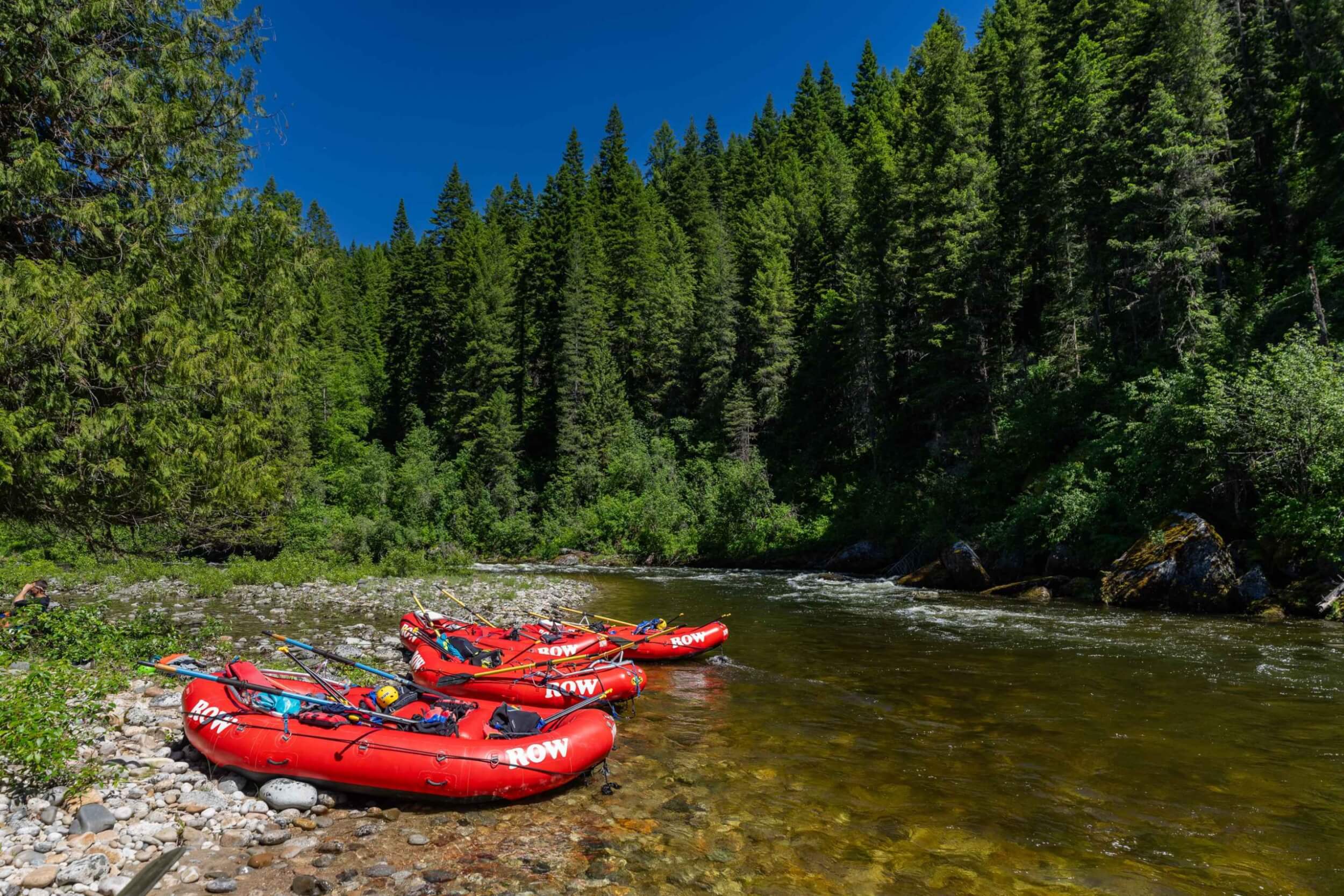 Cluster of red ROW rafts rest on the rocky shore beside calm river water