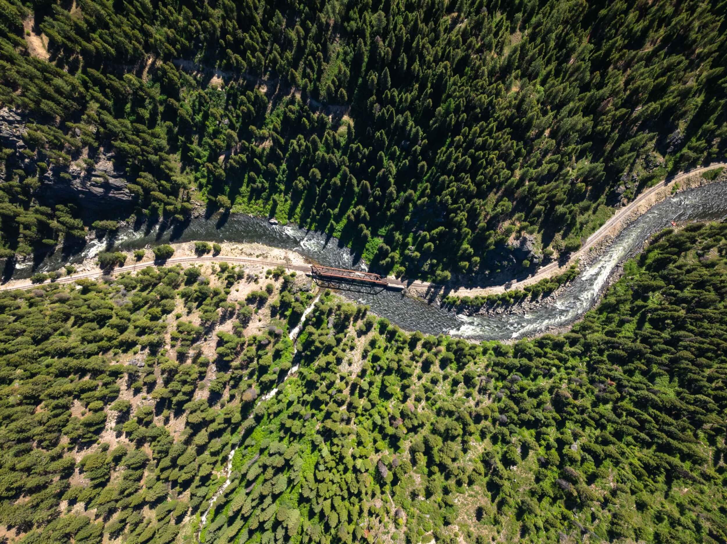 Aerial view of the Main Fork of the Payette River winding through a forest with a bridge crossing the water.