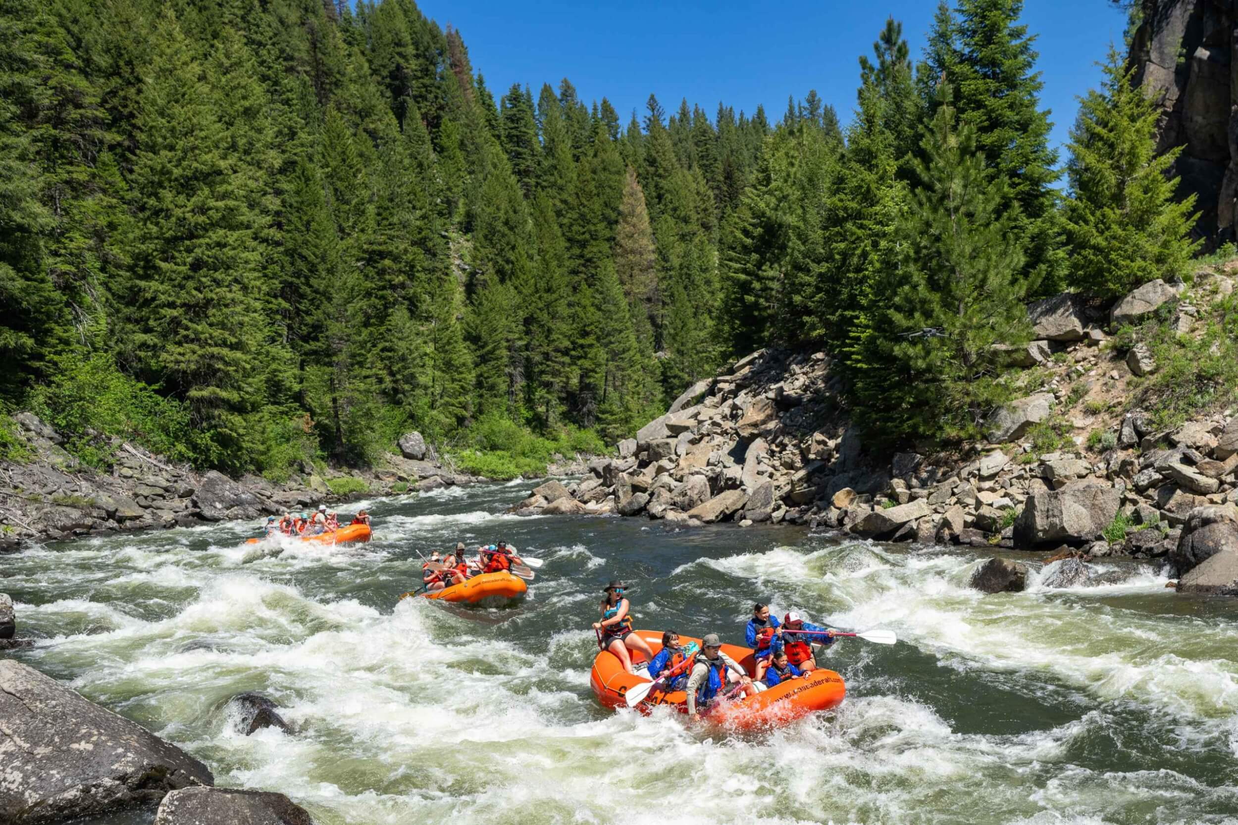 A flotilla of orange rafts with paddlers navigating whitewater on the Payette River.