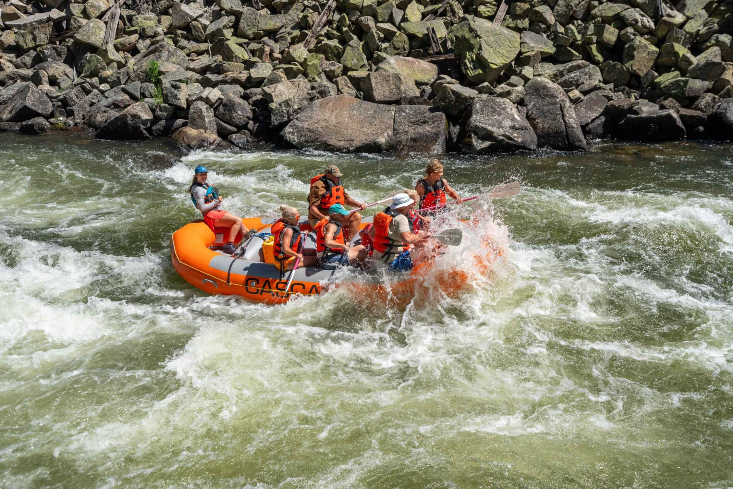 A group of people in an orange raft getting splashed while navigating whitewater rapids on the Payette River.