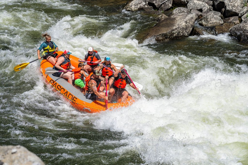 A whitewater rafting group rides on orange raft, charging across the Payette River.
