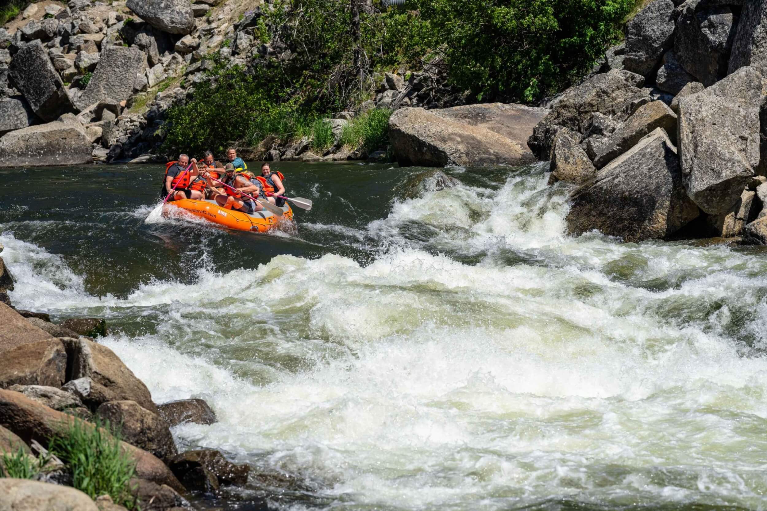 A raft approaches a large drop on the Payette River surrounded by rocks and foamy water.