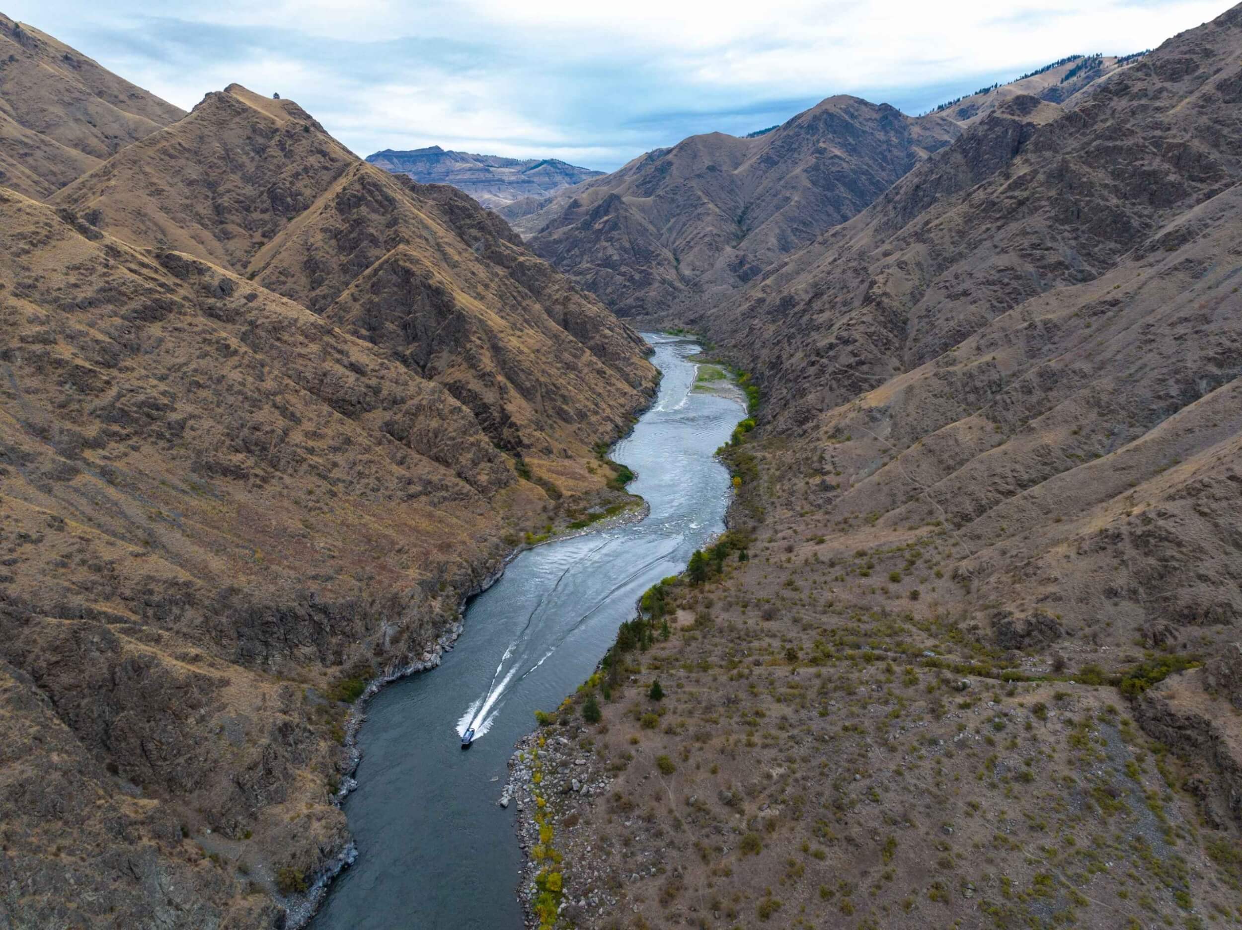 Jet boat weaving through rapids in Hells Canyon with rocky cliffs in view.