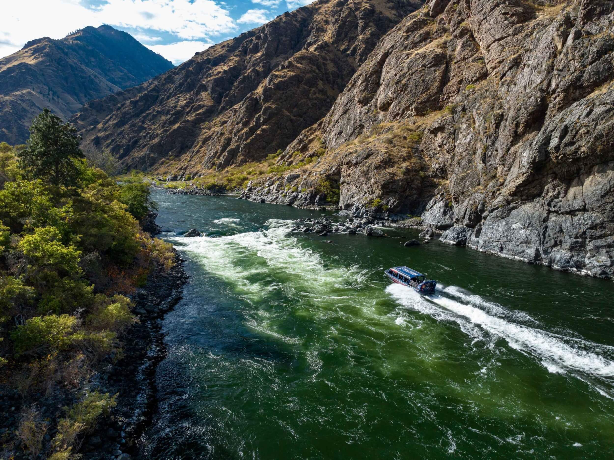 Jet boat cruising upstream through Hells Canyon on emerald-green water.