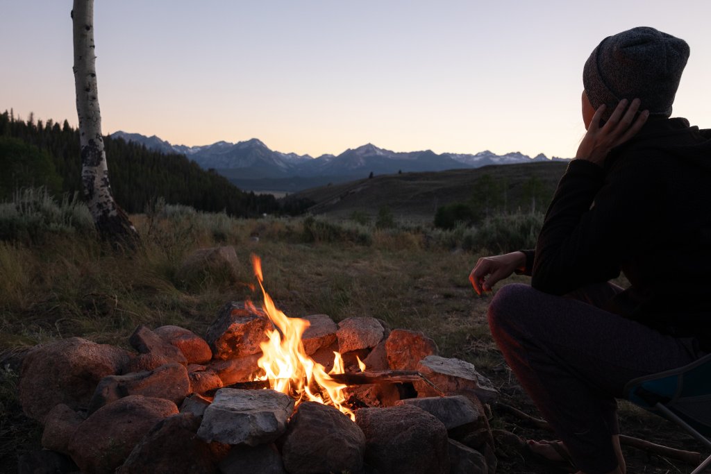 TRAVEL WITH CARE: CAMPFIRE SAFETY A person sits next to a campfire.