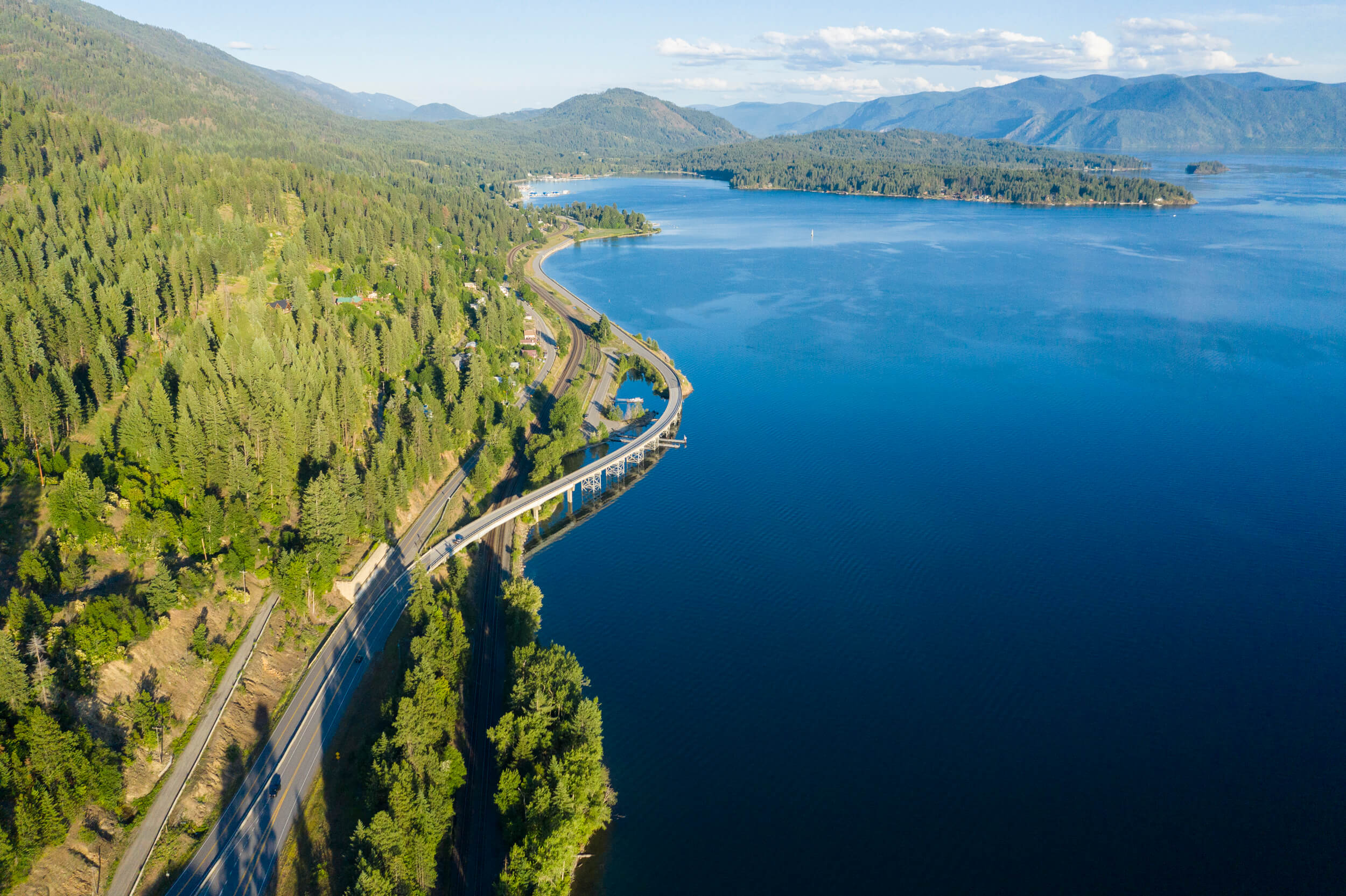 Try These 7 Scenic Byways to Find Natural Wonders The Lake Pend Oreille Scenic Byway between a tree-covered mountain and Lake Pend Oreille.