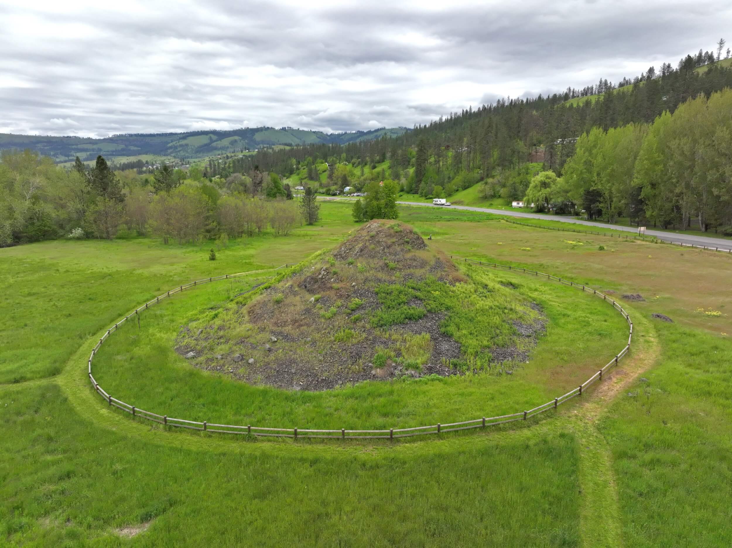 Try These 7 Scenic Byways to Find Natural Wonders An aerial view of the Heart of the Monster site, surrounded by a sprawling field and a tree-covered hill off to the side.