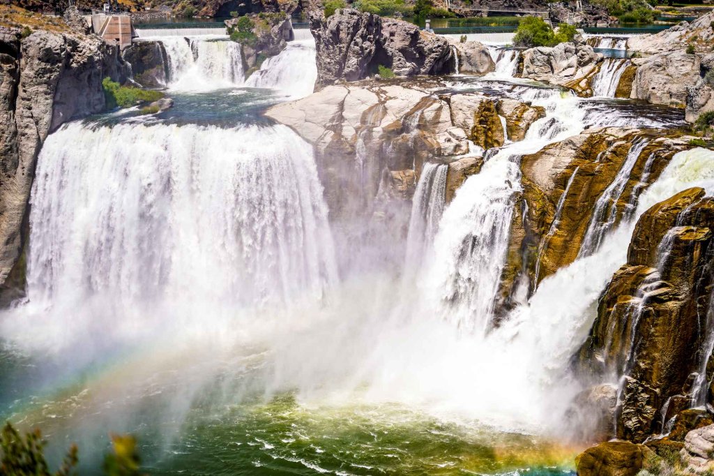 Powerful waterfalls cascade over layered rock at Shoshone Falls near Twin Falls, with a rainbow in the mist.