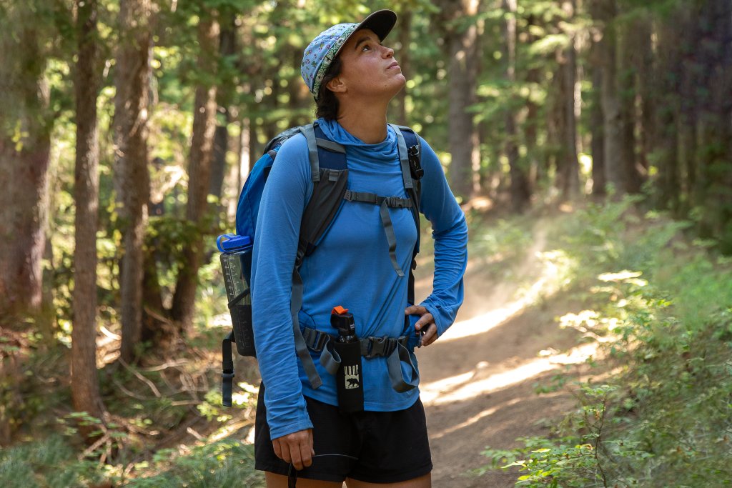 TRAVEL WITH CARE: HIKING RESPONSIBLY A hiker in blue wears bear spray strapped to their waist.