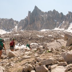 Hikers follow a rocky trail to a snowy summit.