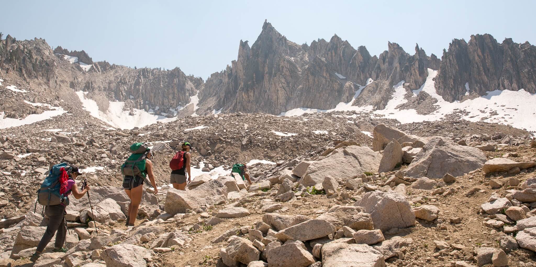 Hikers follow a rocky trail to a snowy summit.