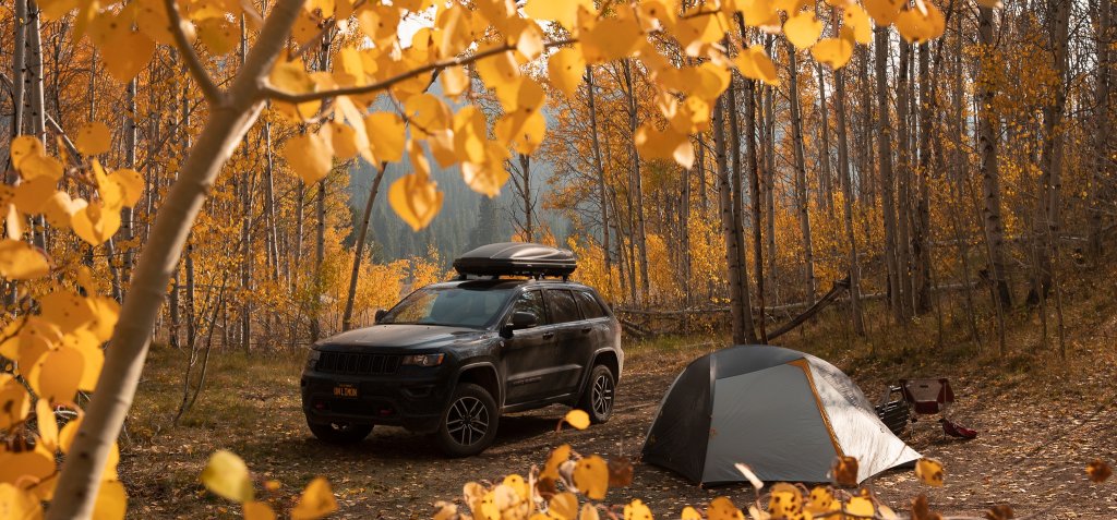 A car and tent set up in a forest clearing surrounded by golden aspens.