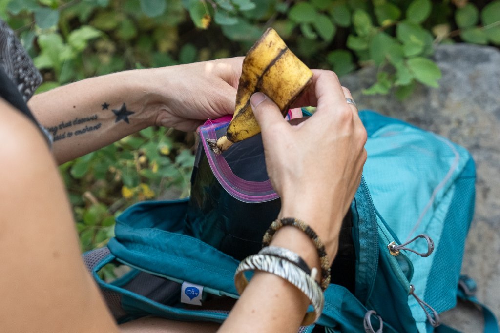 TRAVEL WITH CARE: HIKING RESPONSIBLY A hiker packs out a banana peel in a trash bag instead of littering on the trail.