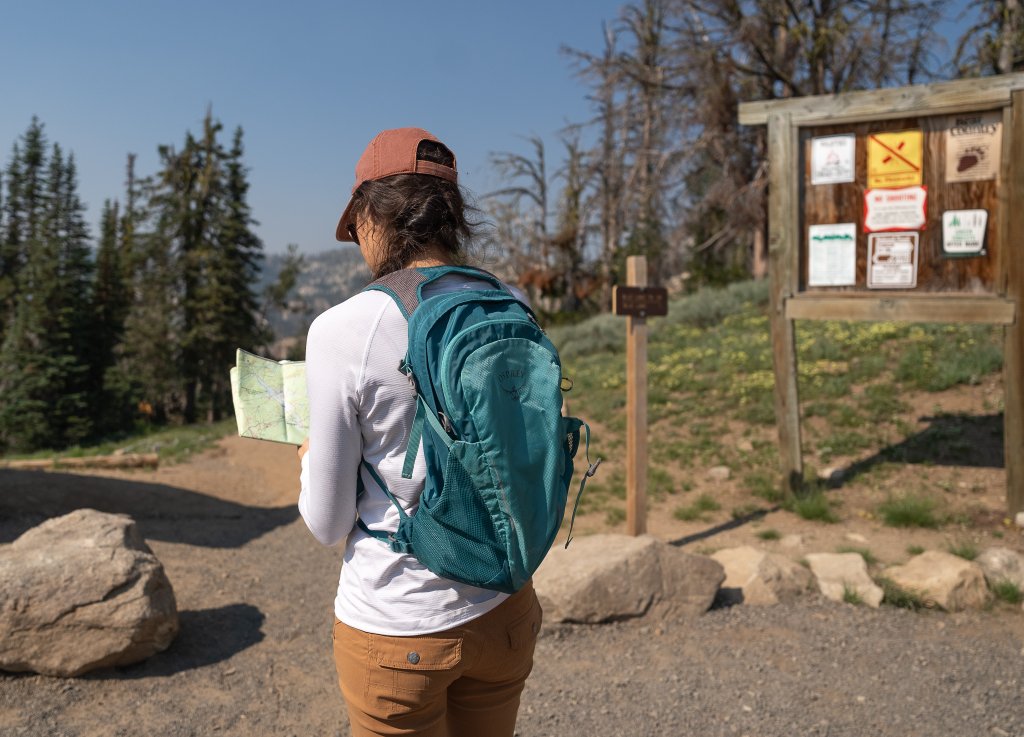 TRAVEL WITH CARE: HIKING RESPONSIBLY A hiker carrying a blue backpack looks over a map before traversing the trail.