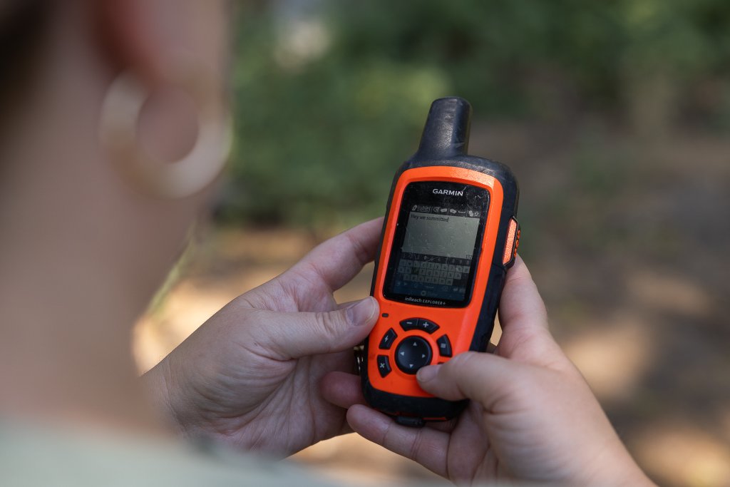 TRAVEL WITH CARE: HIKING RESPONSIBLY A hiker sends a message on an orange satellite communication device.