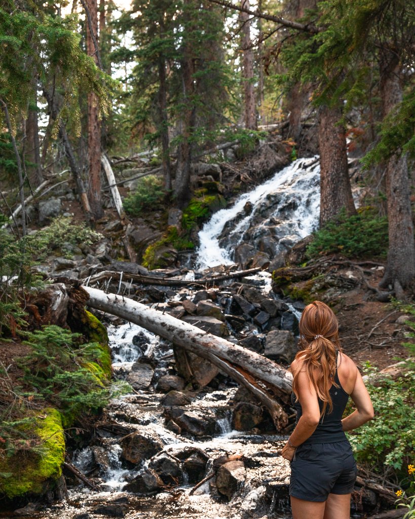 TRAVEL WITH CARE: HIKING RESPONSIBLY A hiker with red hair watches water cascade down a mountainside.