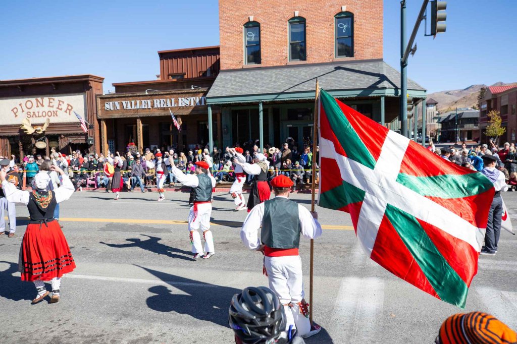 A group of Basque dancers performing in a parade on a street lined with buildings and spectators.