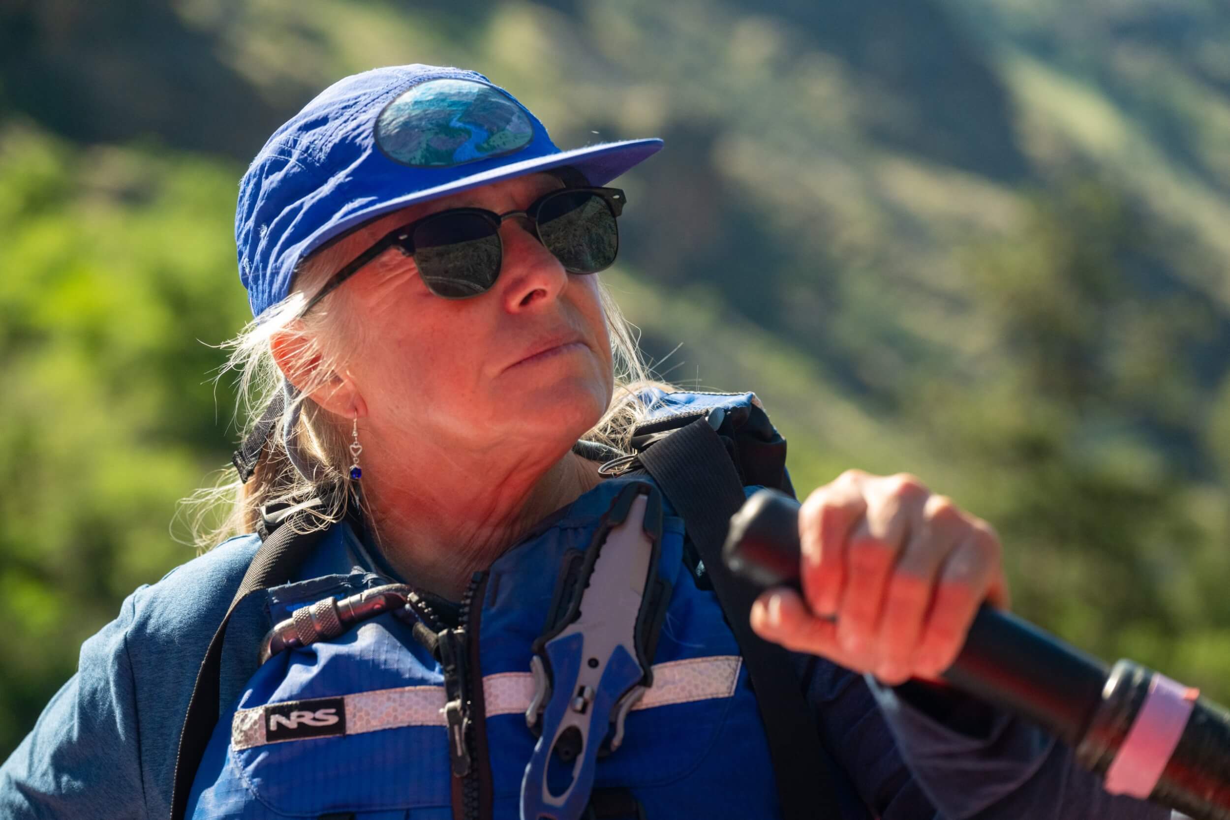 Meet the Queen of the Snake River A woman wearing a blue baseball cap, blue life vest and sunglasses looks off into the distance.