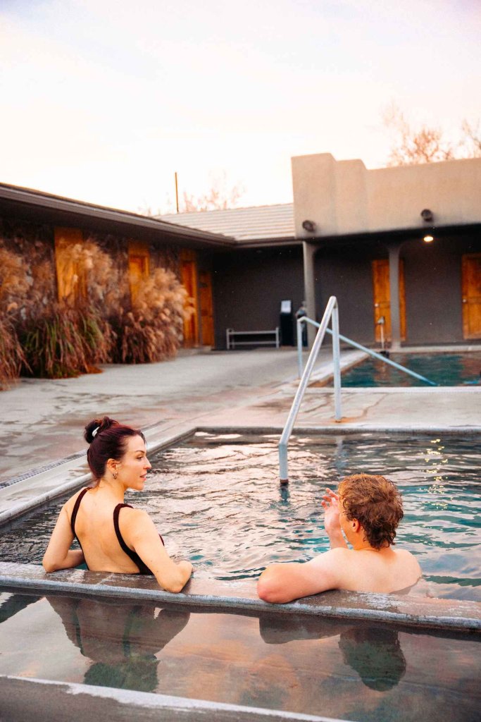 Couple soaking in a steaming outdoor pool at Miracle Hot Springs with fall grasses nearby.