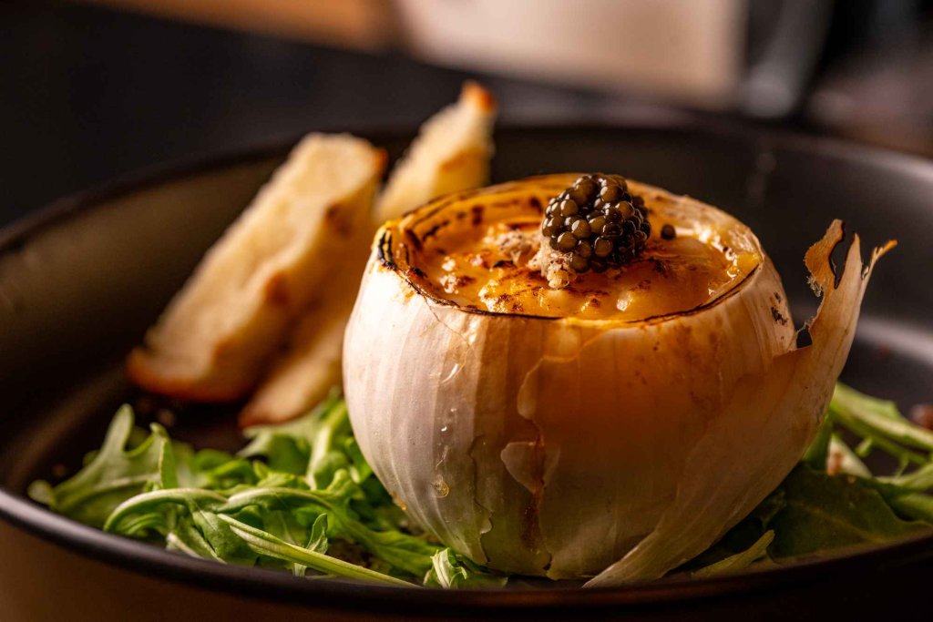 Close-up of an elegant dish served in a roasted onion, garnished with blackberries and paired with fresh greens.