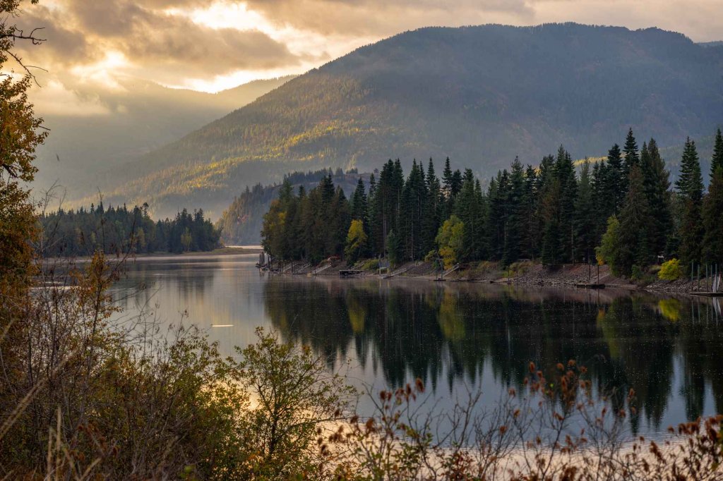 Tranquil mountain lake surrounded by evergreen trees and glowing hillsides near Schweitzer Mountain at sunset.