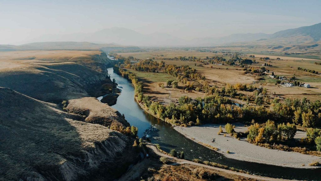Experience the Essence of Fall in Idaho Aerial view of the Salmon River winding through golden plains and rolling hills with mountains in the background.