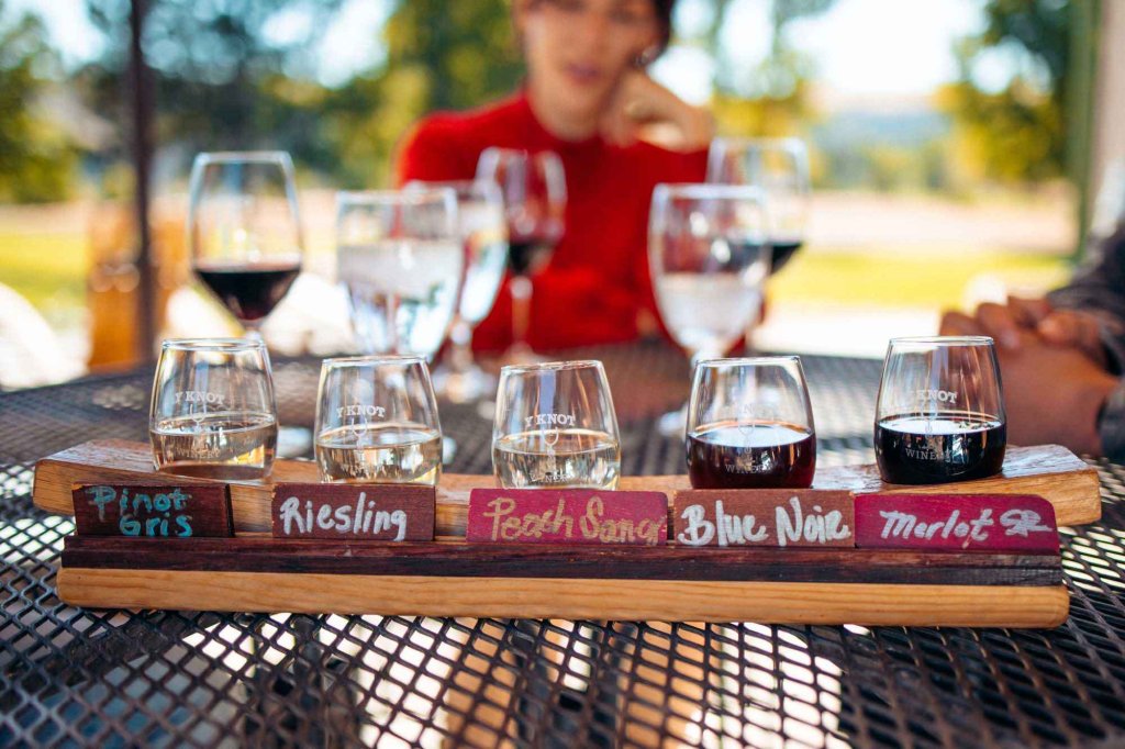 Wine flight featuring five varietals on a wooden tray at Y Knot Winery, with blurred guests in the background.