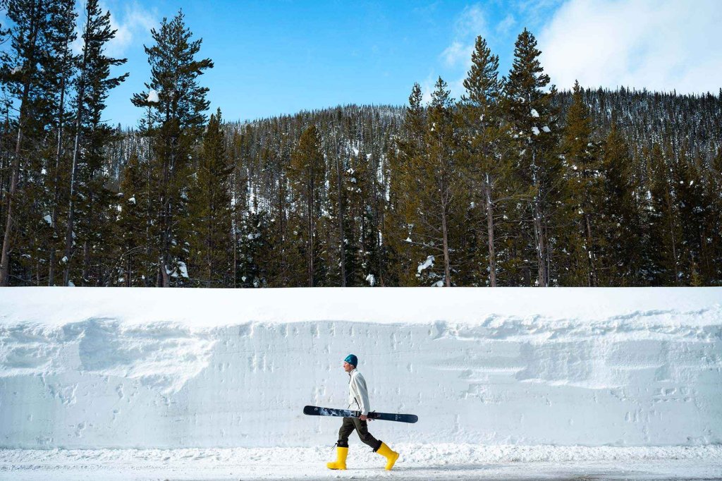 Winter traveler walking along a snow-lined road near Grimes Pass in Southwest Idaho, carrying skis.