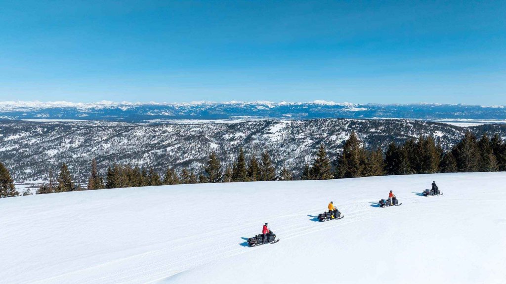 Guided snowmobile group touring a snowy ridgeline near Cambridge, Idaho with panoramic mountain views.