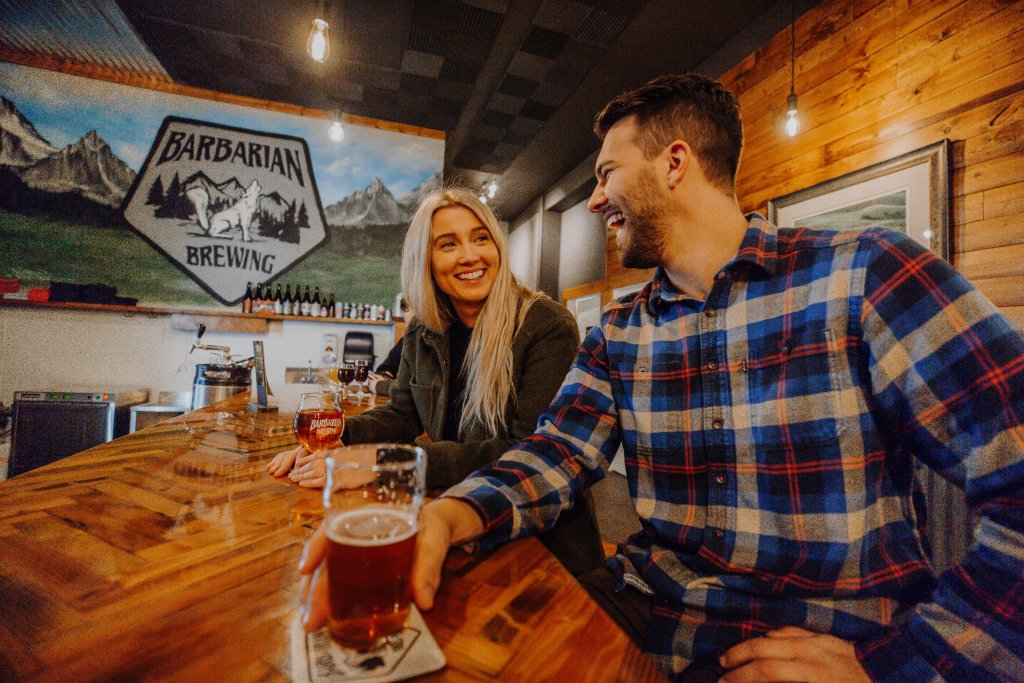 A man and woman seated at a long table with glasses of beer at Barbarian Brewing.