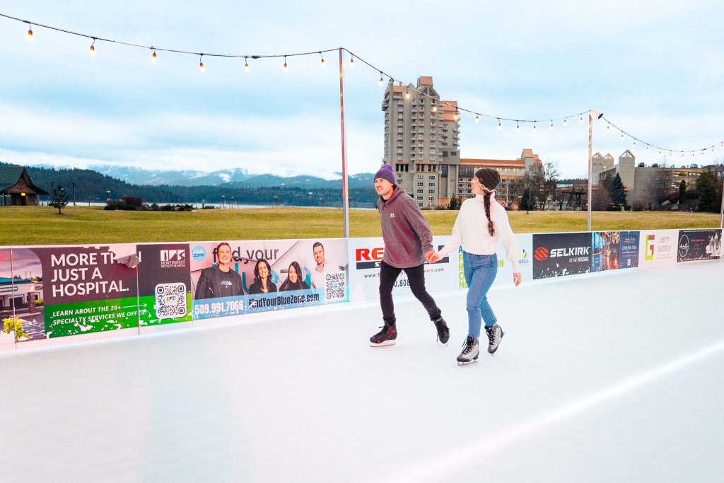 Couple ice skating outdoors at McEuen Park with mountain views in the background