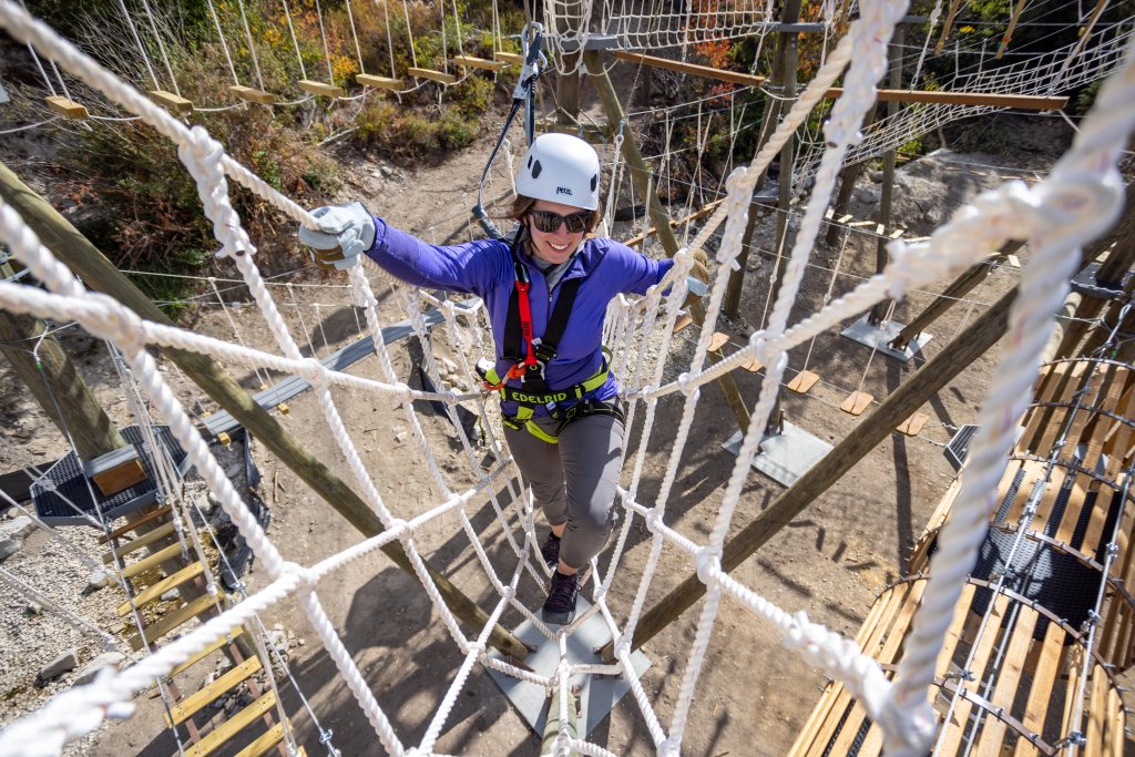 A person wearing a helmet, gloves and sunglasses climbing the Mineshaft Challenge Course at Bogus Basin Recreation Area.